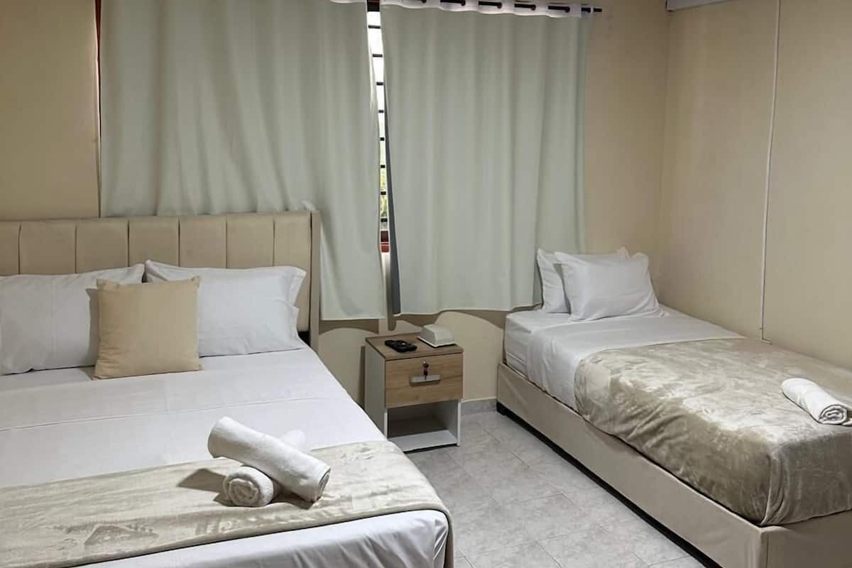 A hotel room with two beds, a nightstand, and a window with curtains.