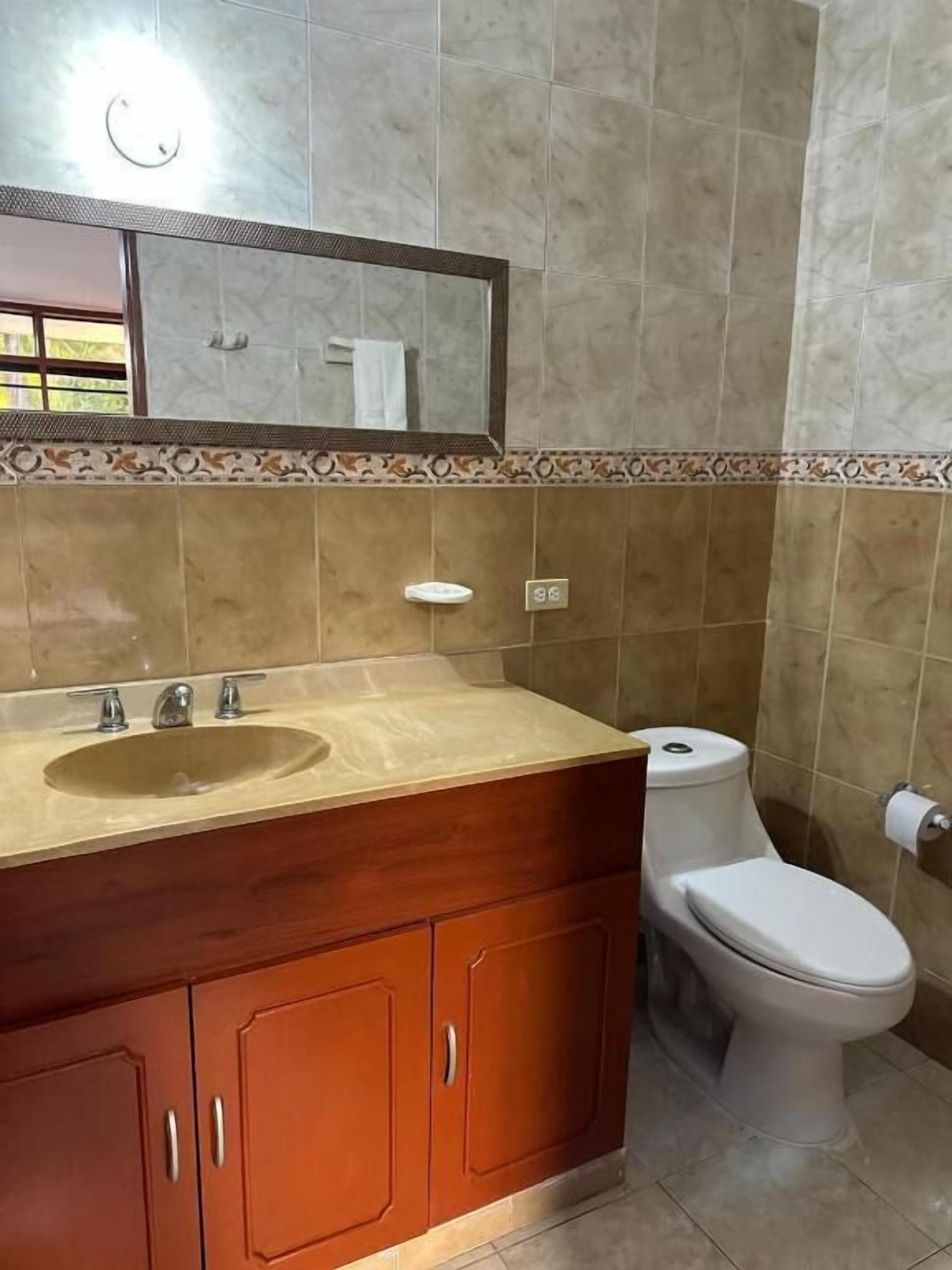 Ein Badezimmer mit einem Holzkosmetikschrank, einem Waschbecken, einem Spiegel, einer Toilette und einem Handtuchhalter.