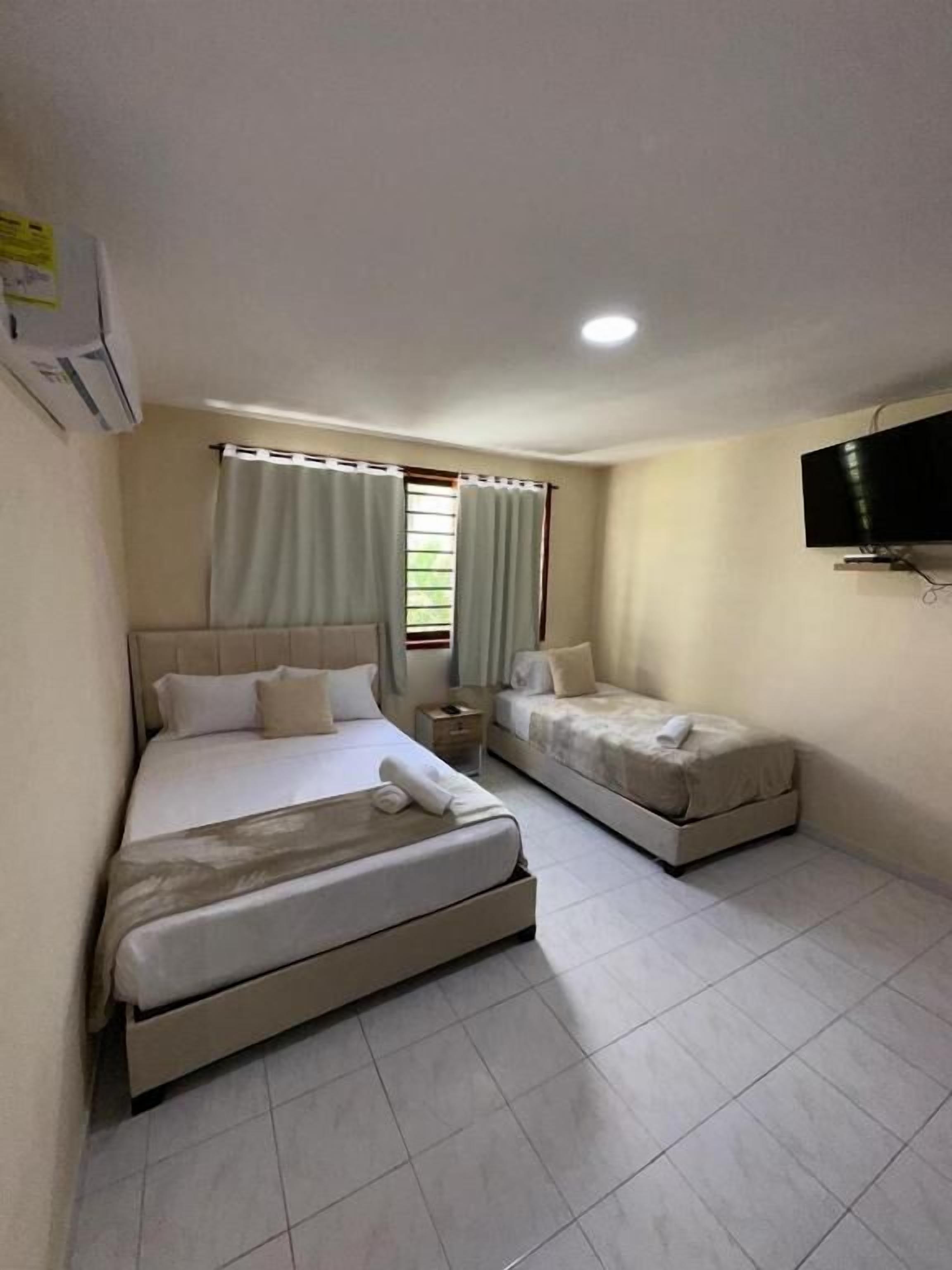 A hotel room with two beds, a TV, and a window with curtains.