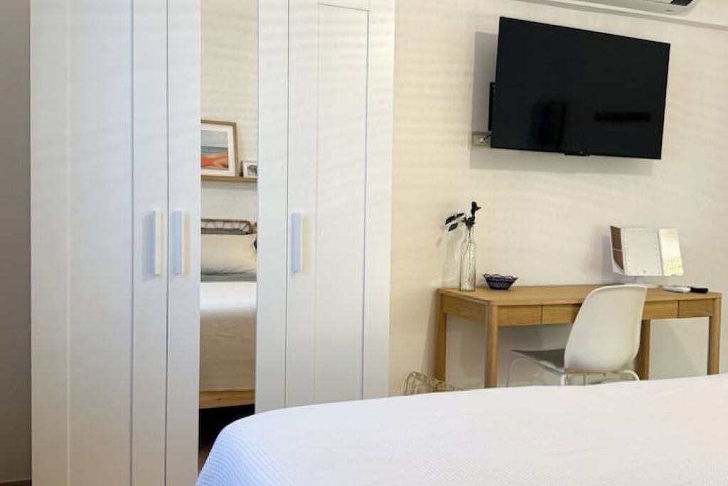 Ein Schlafzimmer mit einem Bett, einem Schreibtisch mit Stuhl, einem an der Wand montierten Fernseher und einem Kleiderschrank.