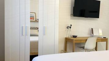 Ein Schlafzimmer mit einem Bett, einem Schreibtisch mit Stuhl, einem an der Wand montierten Fernseher und einem Kleiderschrank.
