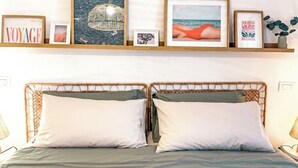 Ein Doppelbett mit zwei Kissen, ein Regal darüber mit gerahmten Bildern und eine Wandleuchte.