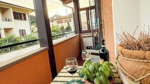 Ein Balkon mit Tisch, zwei Weingläsern, einer Flasche und einem Topf mit Basilikum.
