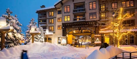 Un hôtel à plusieurs étages, dont l’entrée est recouverte de neige et dont la façade est illuminée.