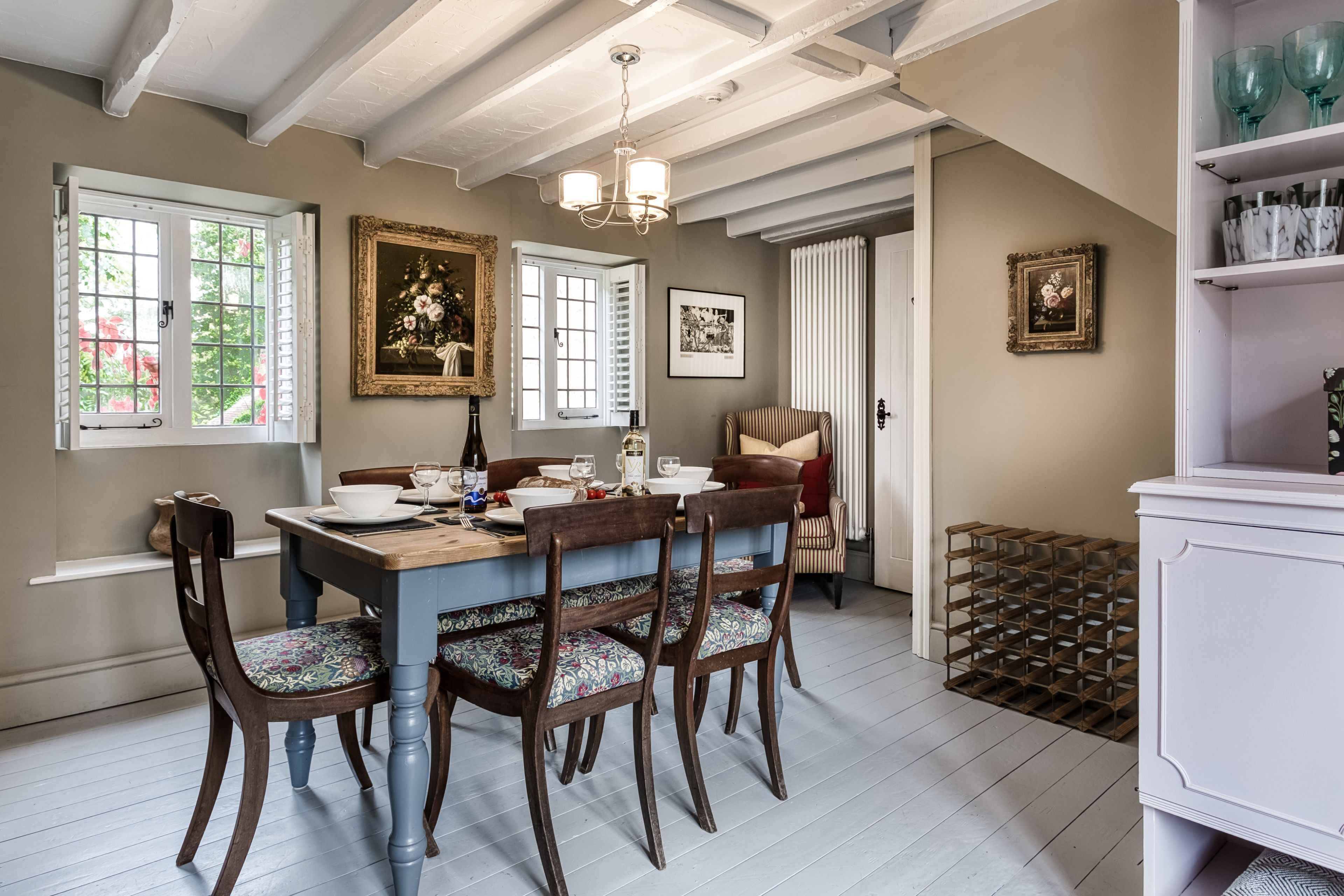 A dining area with a wooden table and chairs, a chandelier, and framed artwork on the walls.