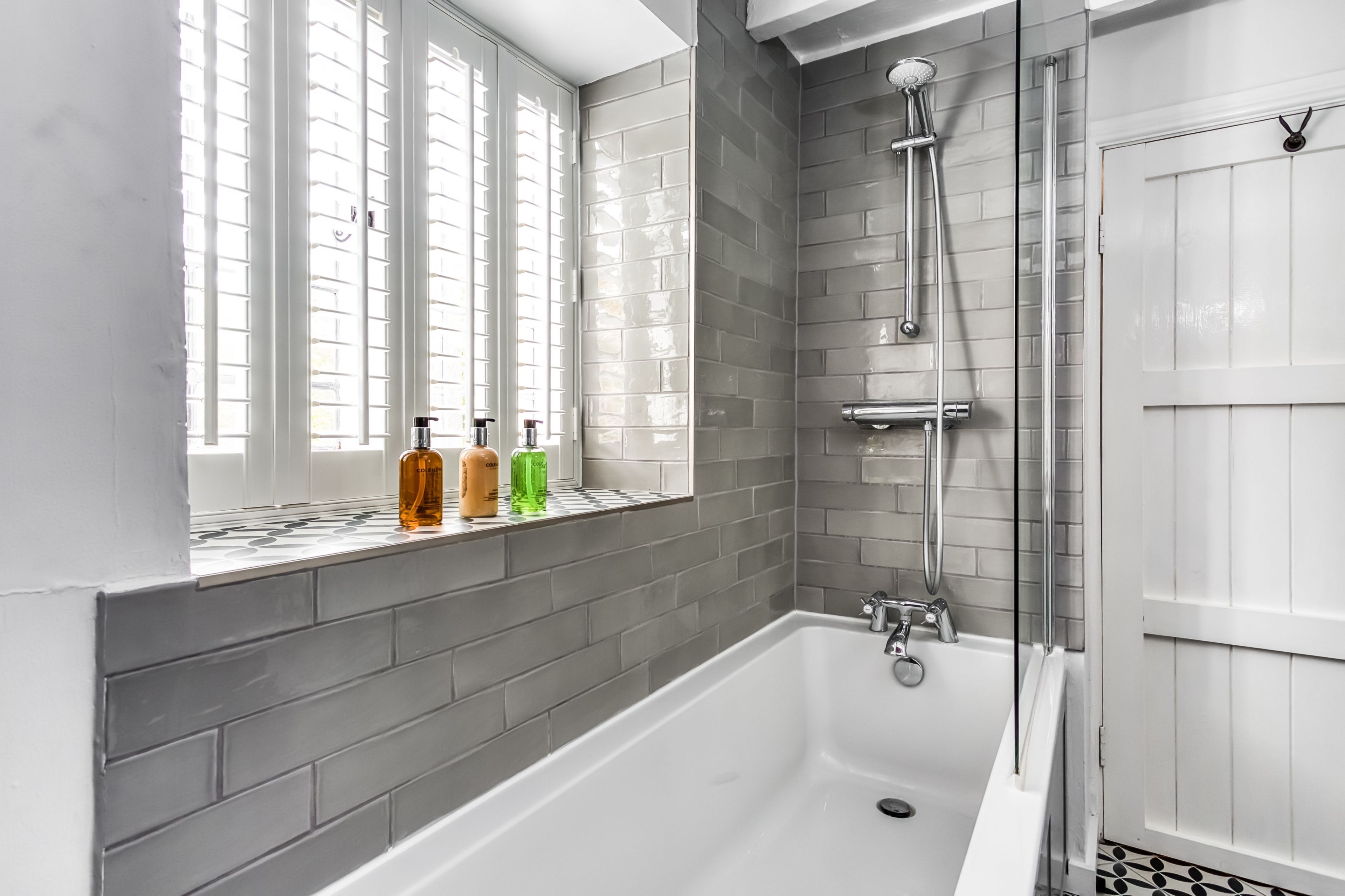 Ein modernes Badezimmer mit einer großen Badewanne, einer Dusche und einem Fenster mit Jalousien.