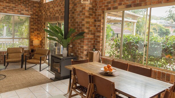 A room with a brick wall, a large window, a table with chairs, and a plant. - Tropic Lodge by Charlesworth (Coffs Harbour)