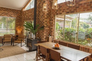 A room with a brick wall, a large window, a table with chairs, and a plant. - Tropic Lodge by Charlesworth (Coffs Harbour)