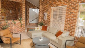 A living room with a brick wall, a sofa, a coffee table, and a chair. - Tropic Lodge by Charlesworth (Coffs Harbour)