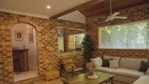 A cozy living room with a brick wall, a wooden coffee table, a sofa, and a ceiling fan. - Tropic Lodge by Charlesworth (Coffs Harbour)