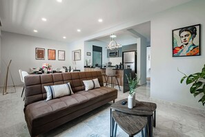 A modern living room with a sofa, a dining area, a kitchen, and a hallway leading to another room. - Amazing 2BR Apt in Roma Norte - Yoga Room (Mexico City)