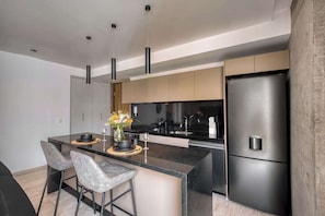 A modern kitchen with a central island, stainless steel appliances, pendant lighting, and a dining area with bar stools. - Stylish 1BR Apartment in Roma Norte Near Condesa (Mexico City)