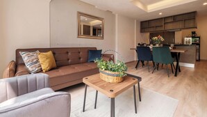 A modern living room with a brown sofa, a small table with a basket, and a dining area with chairs and a kitchen in the background. - Brand New 2 BR Condo in Reforma - Queen Beds (Mexico City)