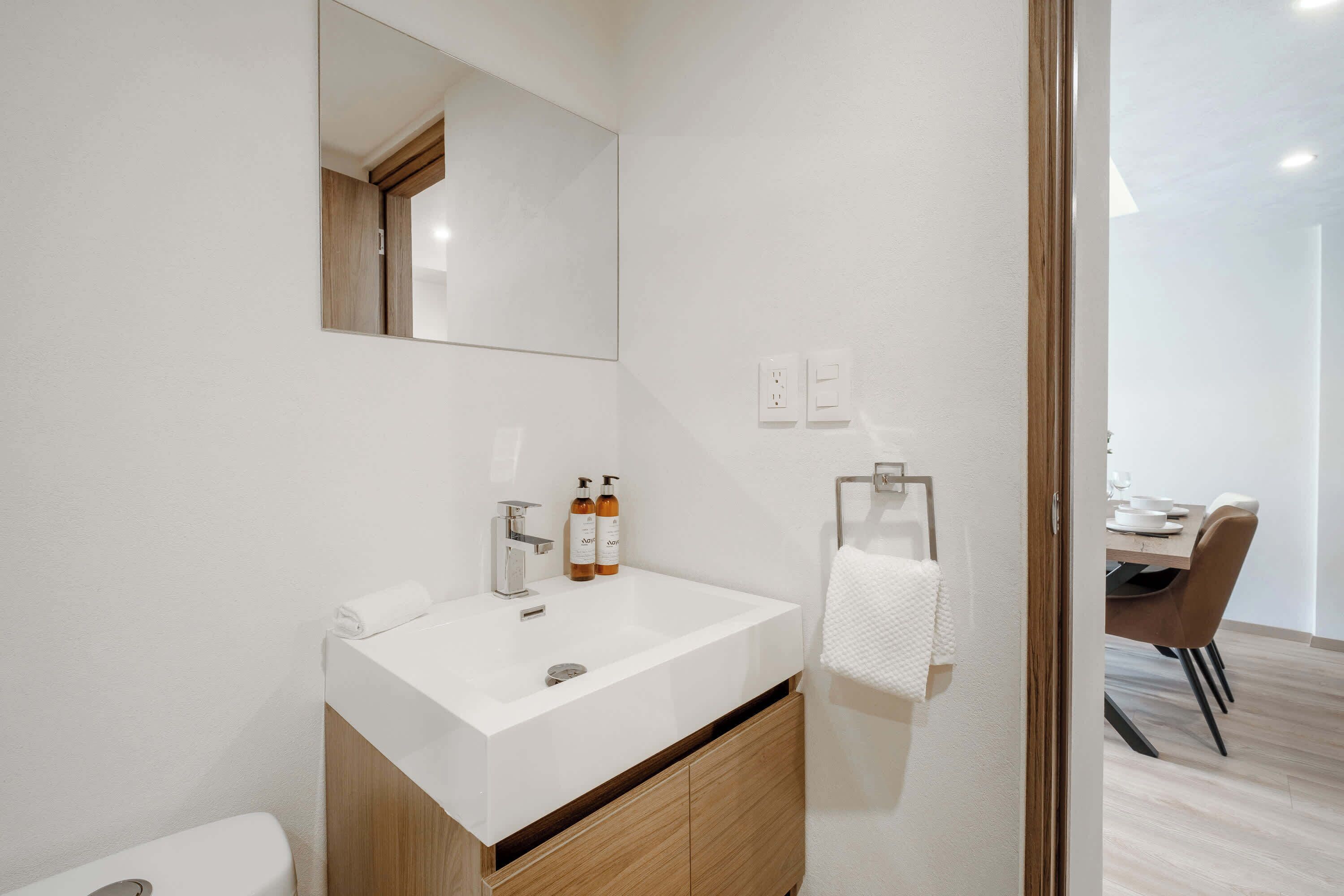 A modern bathroom with a white sink, mirror, and wooden cabinet.