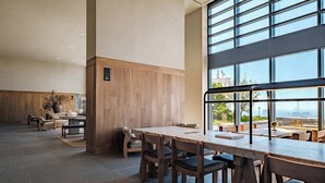 Amplo espaço interno com uma grande mesa e cadeiras, painéis de madeira nas paredes e janelas amplas com vista.