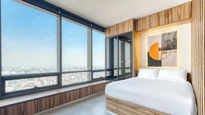 Quarto com uma grande janela, cama e vista para a cidade.