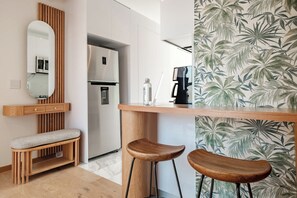Eine moderne Küche mit einer hölzernen Bank, zwei Hocker, einem Kühlschrank und einer Kaffeemaschine.