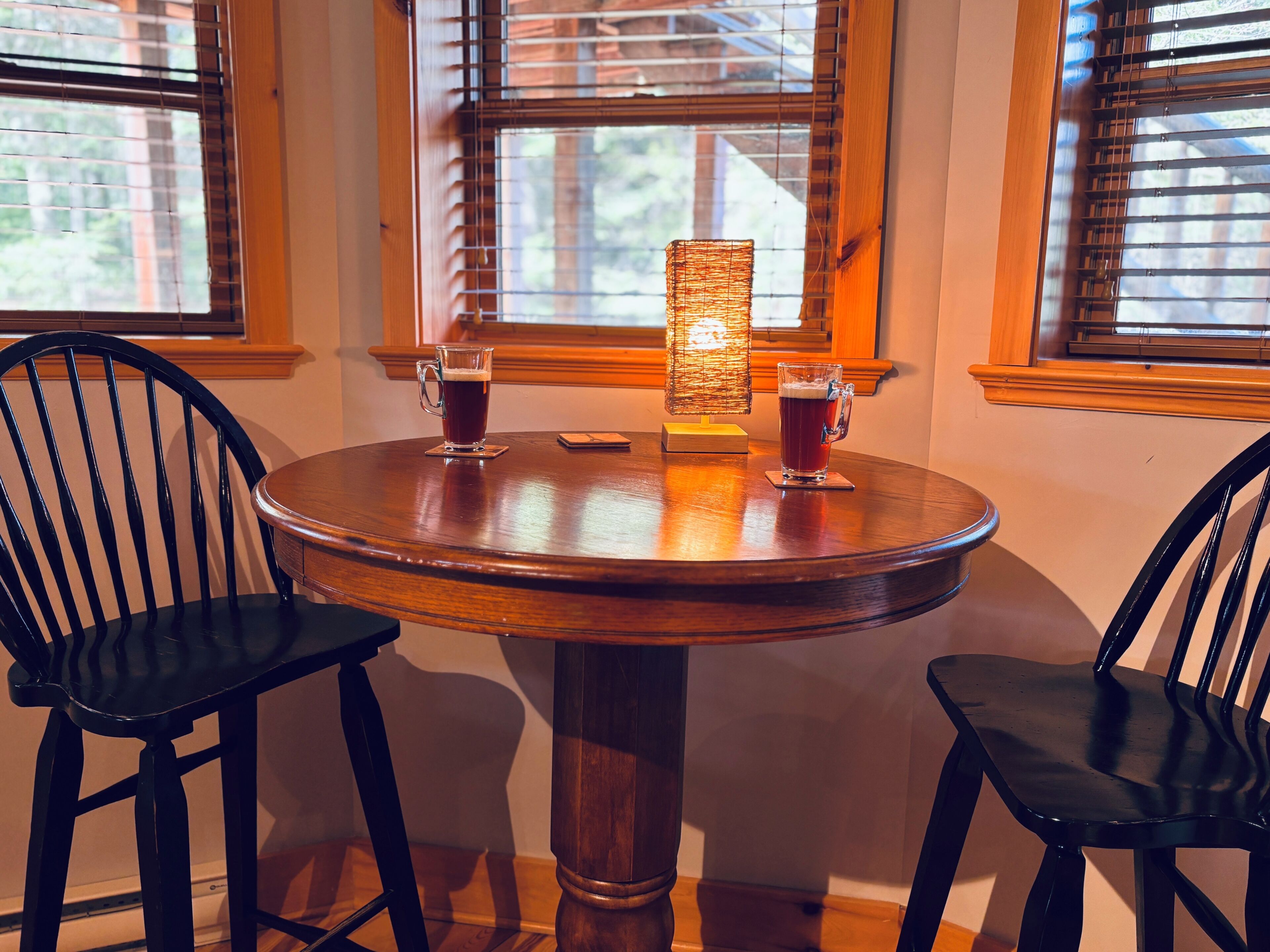 A round wooden table with two chairs, two glasses of beer, and a candle in the center.