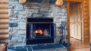 A stone fireplace with a 'HOME' sign above, a wooden mantel shelf, and two glasses of orange juice on a wooden table. - Chal’Heureux | Private Spa, Log Cabin Retreat at Lac Fiddler | Dog Friendly (Mille-Isles)