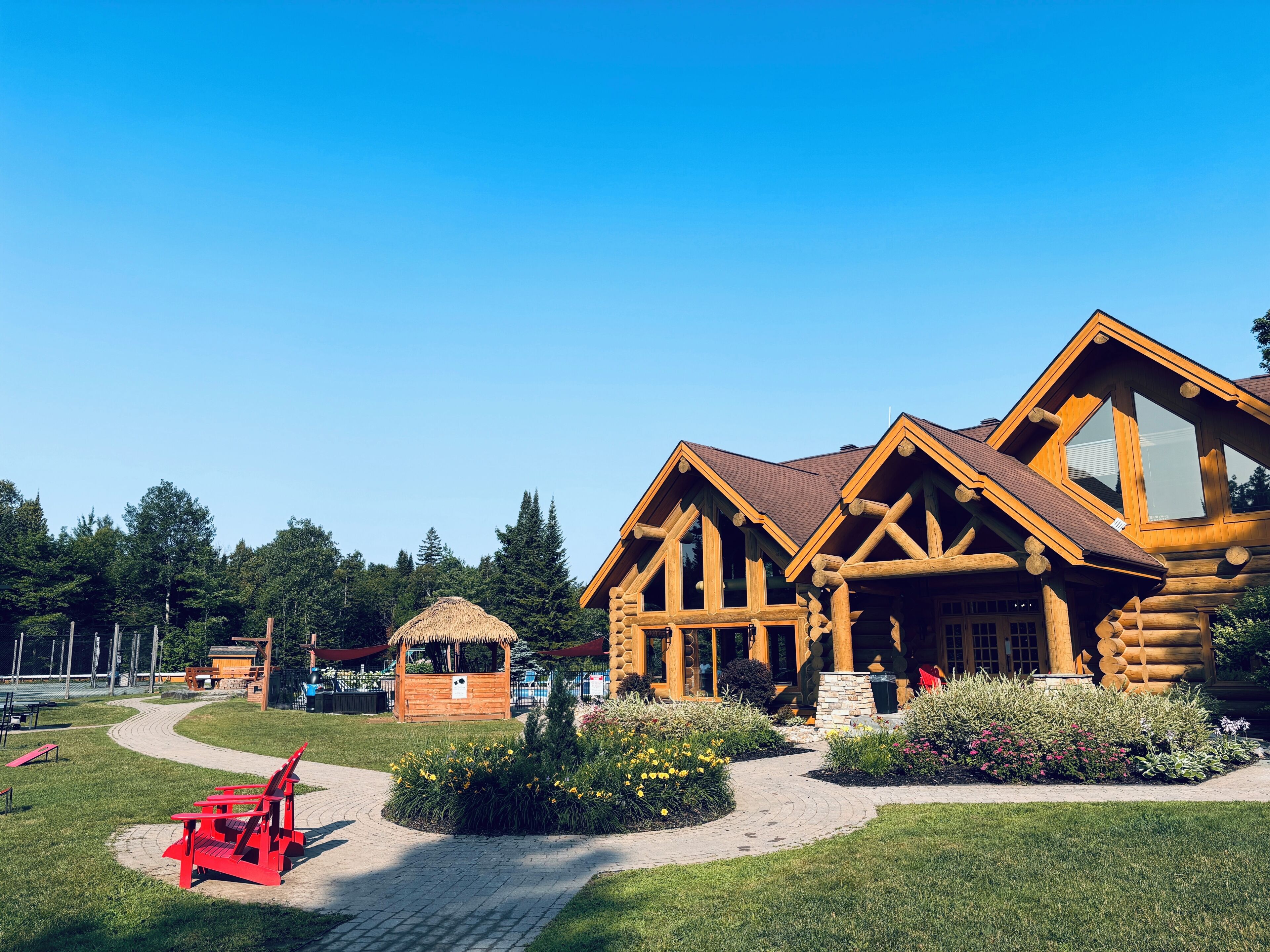 Un bâtiment de style cabane en rondins, avec un chemin pavé, une chaise rouge et une petite construction en arrière-plan.
