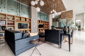A modern living room with a sofa, a black armchair, a TV, wooden shelves, and hanging lights. - Redesigned 1BR Condo in Polanco - Pool Gym - Padel (Mexico City)