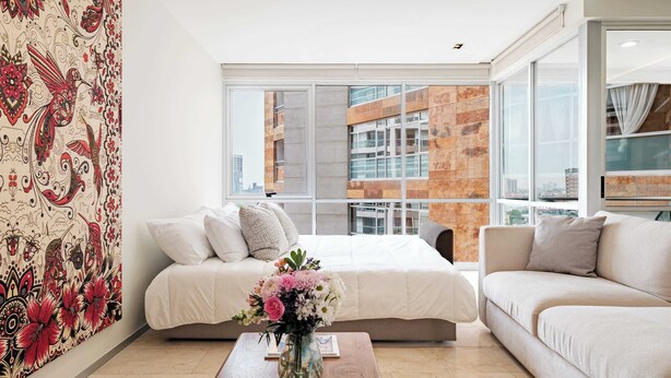 Quarto moderno com uma grande janela, uma cama, um sofá e uma parede decorativa.