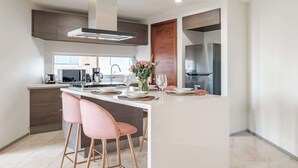 Uma cozinha moderna com uma ilha central, banquetas, geladeira de aço inoxidável e forno embutido.