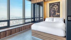 A bedroom with a large bed, a city view through floor-to-ceiling windows, a wooden panel wall, and a framed artwork above the bed. - Luxury Studio - Pool - Revolution Monument View (Mexico City)