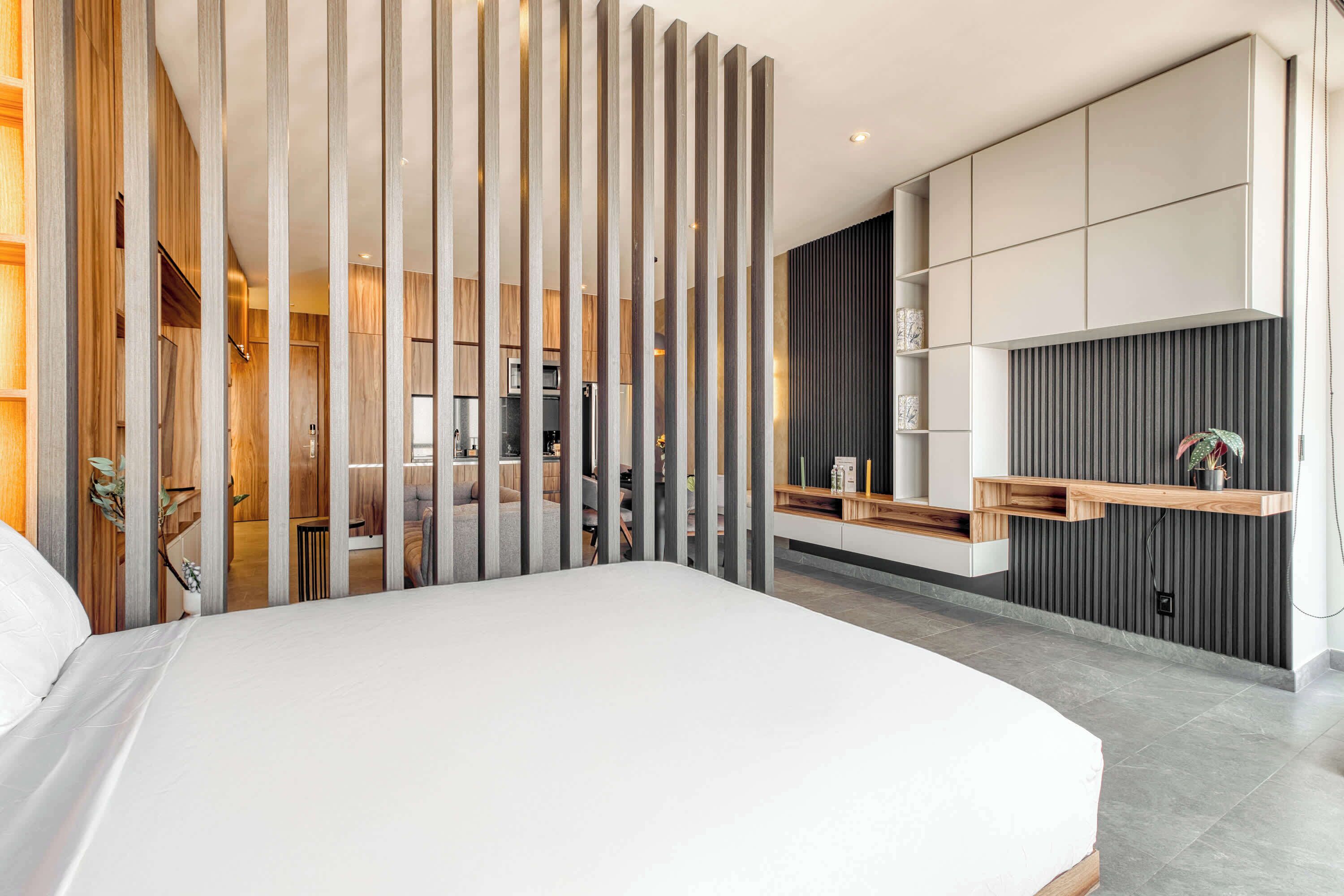 A modern bedroom with a large bed, a wooden partition, and a built-in kitchen area.