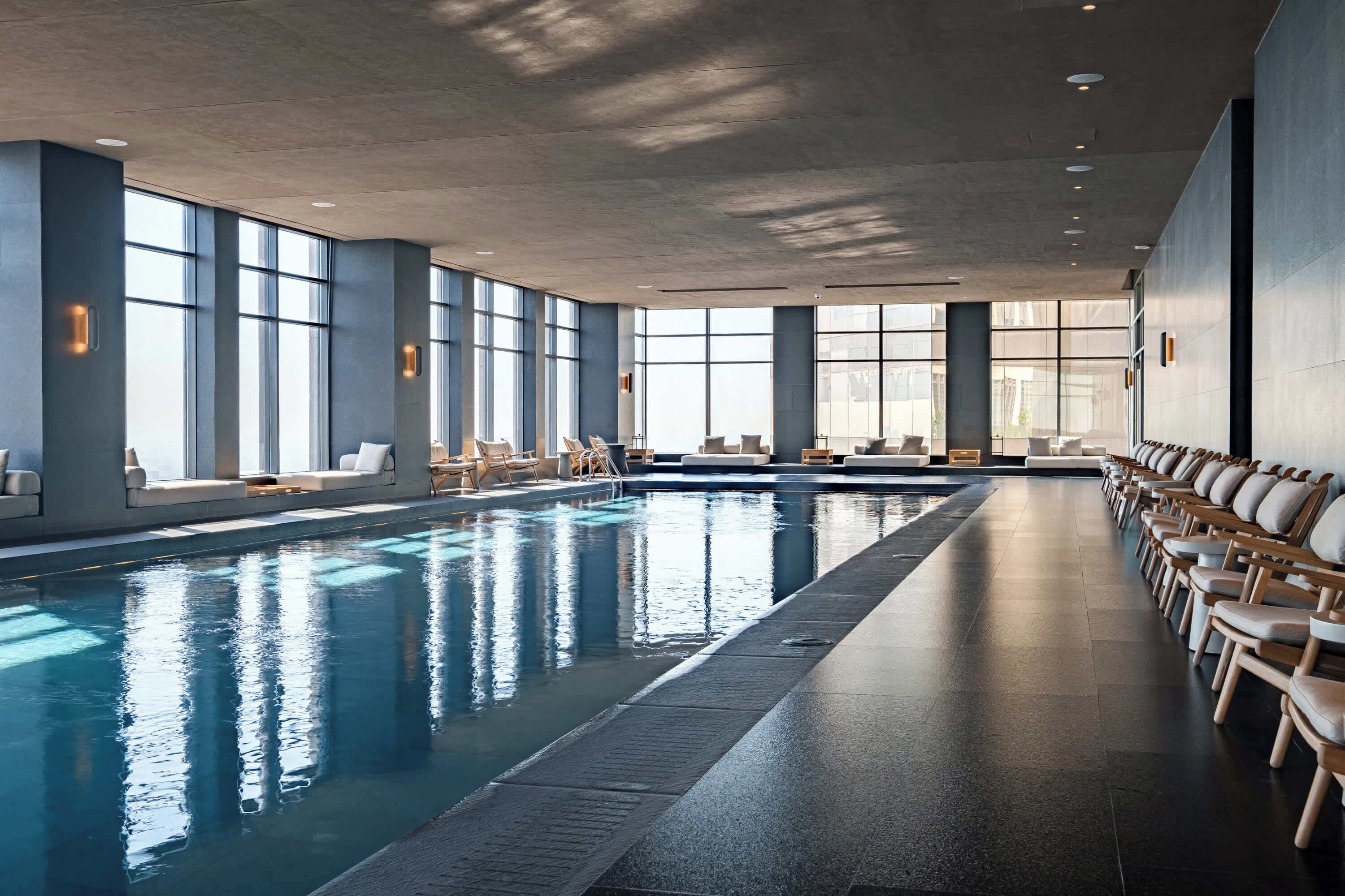 A large indoor swimming pool with lounge chairs and sun loungers along the sides.