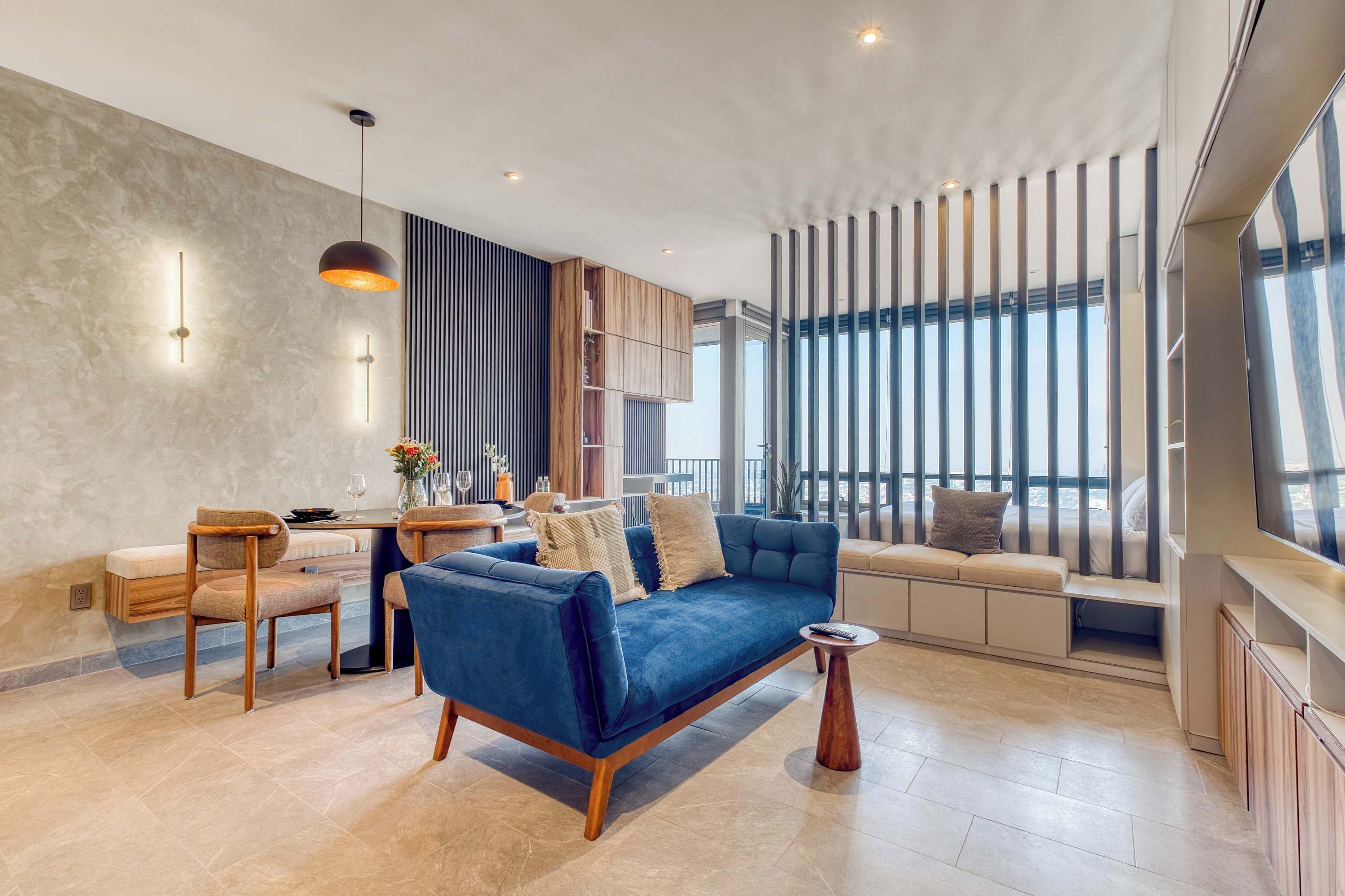 A modern living room with a blue sofa, wooden chairs, a small table, and a TV.