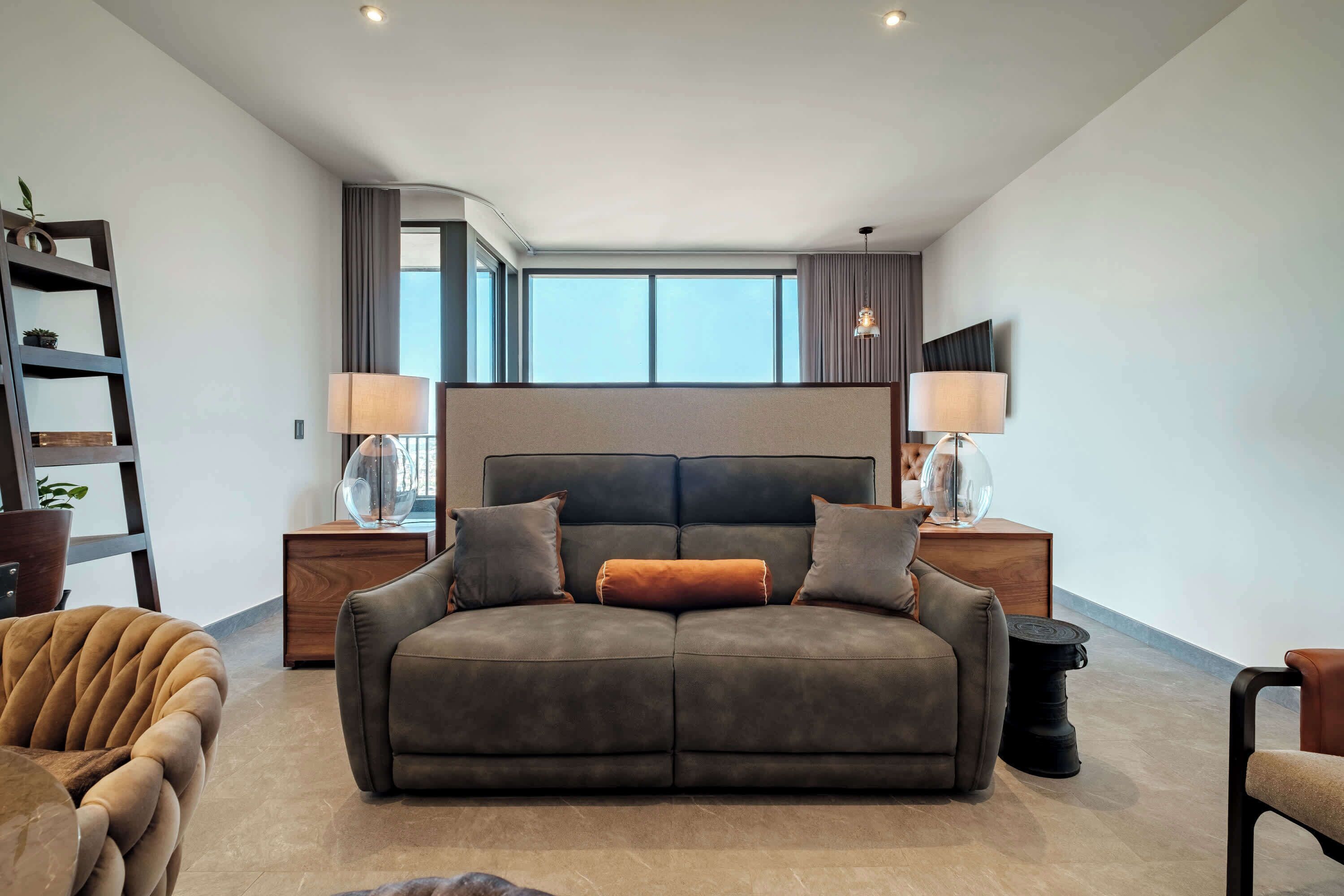 Ein modernes Schlafzimmer mit einem großen Bett, zwei Nachttischen mit Lampen, einem Sofa und einem Sessel.