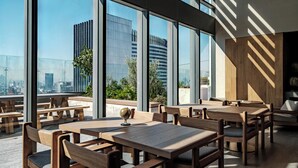 Ein Dachterrassenrestaurant mit Holztischen und -stühlen, großen Fenstern und Blick auf die Stadt.