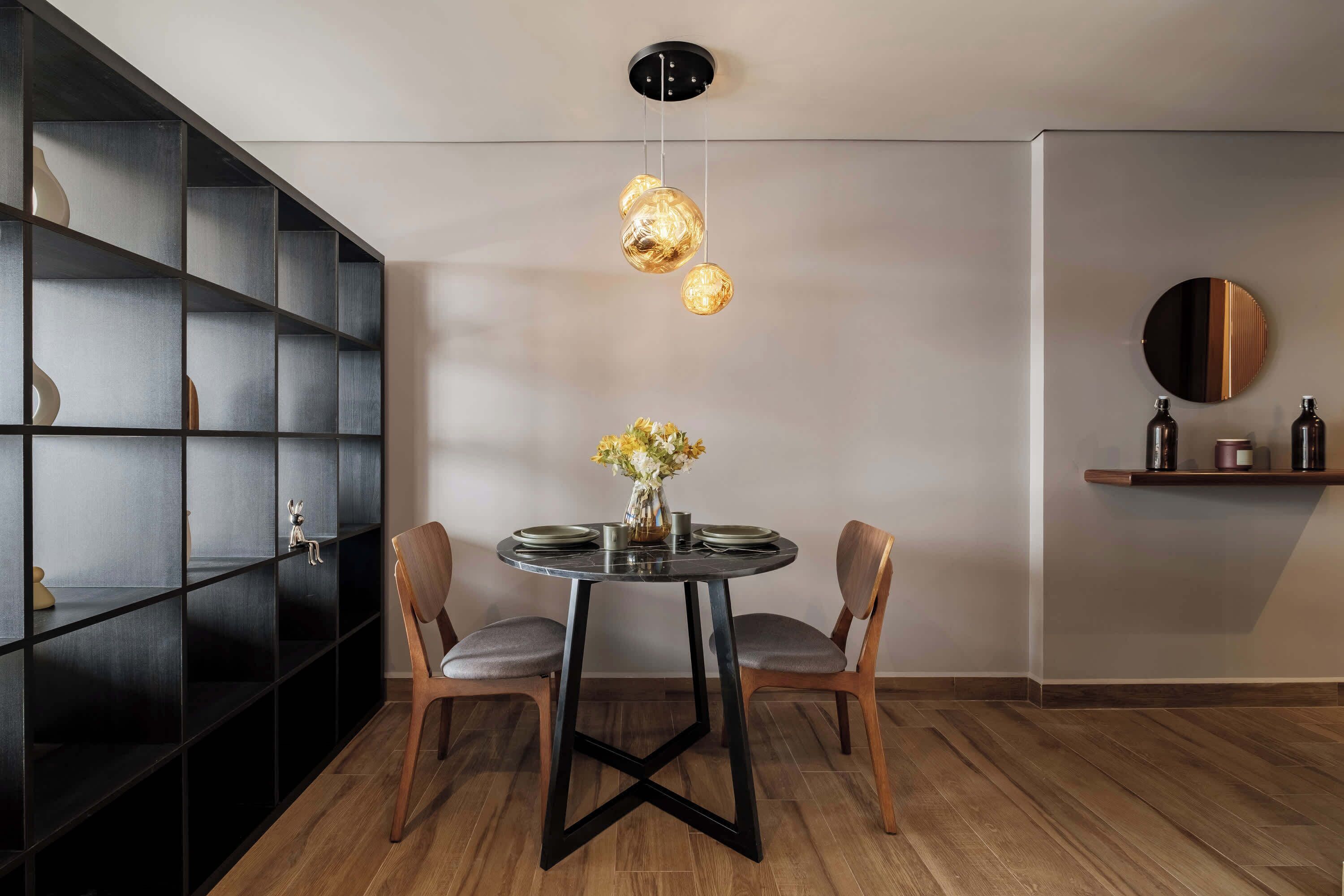 A dining area with a round table, two chairs, a vase with flowers, and a black shelving unit.