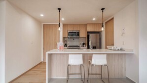 Una cocina moderna con armarios de madera, una isla central con dos taburetes de bar, un microondas y un refrigerador.