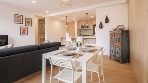 Una sala moderna con un sofá, una mesa de comedor preparada para cuatro personas y una cocina al fondo.
