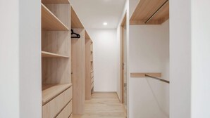 Un pasillo estrecho con estanterías de madera y un perchero, que conduce a una puerta.