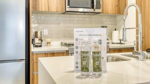 A kitchen with wooden cabinets, a stainless steel microwave, a modern faucet, and a counter displaying two bottles of water. - Luxury 2 BR Condo - Rooftop Pool With City View (Mexico City)