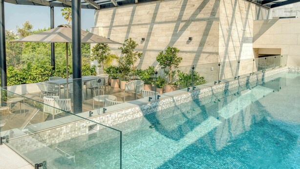 A modern indoor swimming pool with glass railings, potted plants, and outdoor seating. - Luxury 2 BR Condo - Rooftop Pool With City View (Mexico City)