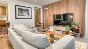 A modern living room with a large flat-screen TV, a sofa, a coffee table, and a wooden accent wall. - Luxury 2 BR Condo - Rooftop Pool With City View (Mexico City)