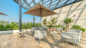 An outdoor patio with tables and chairs, a glass ceiling, and potted plants. - Luxury 2 BR Condo - Rooftop Pool With City View (Mexico City)