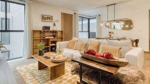 A modern living room with a sofa, coffee table, and a dining area with a mirror and pendant lights. - Luxury 2 BR Condo - Rooftop Pool With City View (Mexico City)