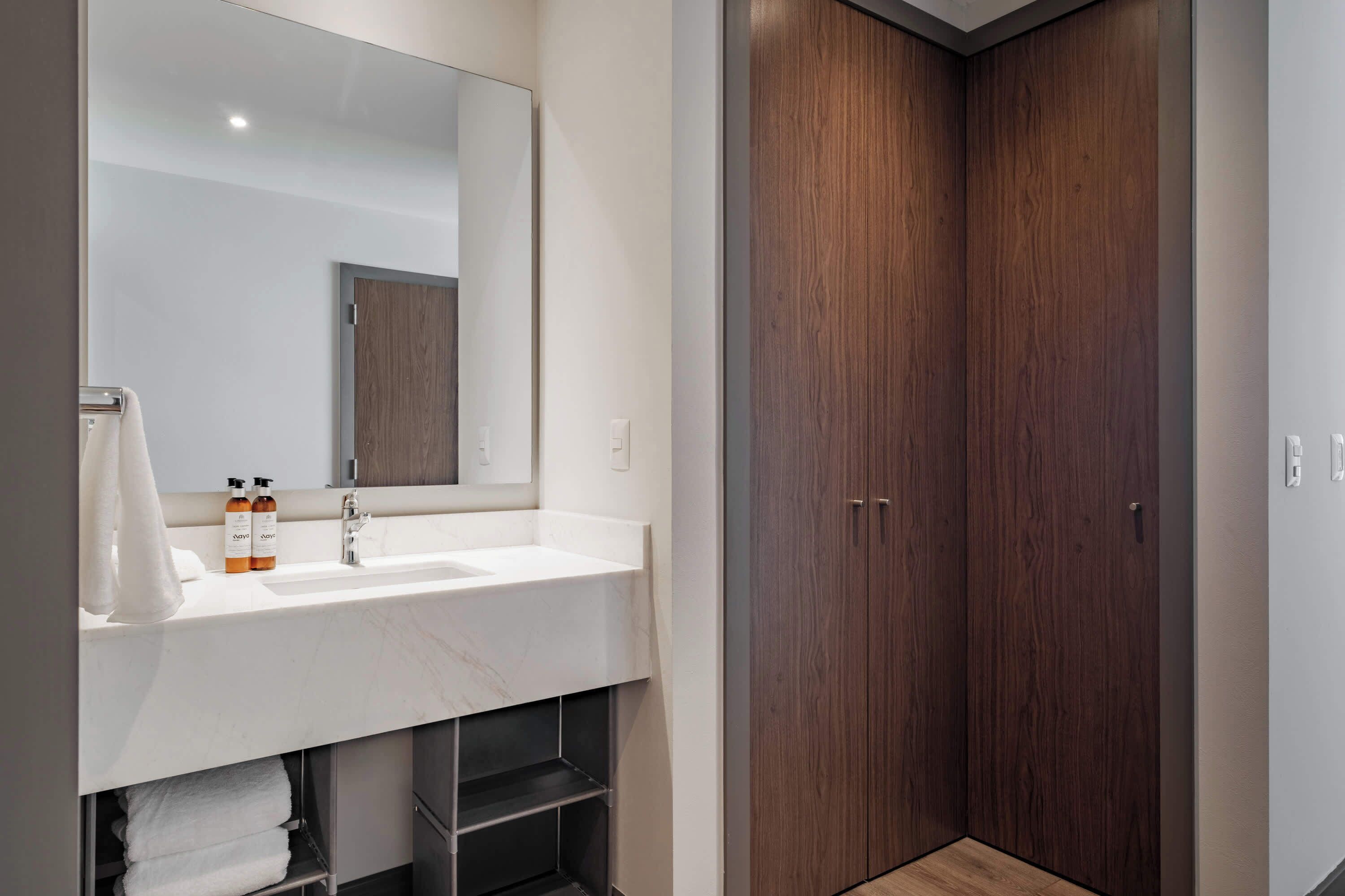 Un baño moderno con un lavamanos blanco, espejo y armario de madera.