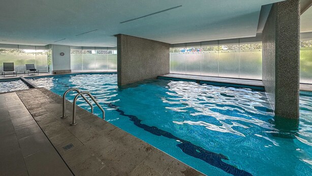 Une piscine intérieure à l’eau claire, dotée d’un plongeoir et offrant une vue sur un paysage verdoyant grâce à de grandes fenêtres.
