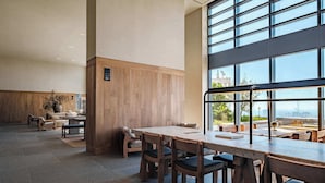 Amplo espaço interno com uma grande mesa e cadeiras, painéis de madeira nas paredes e janelas amplas com vista.
