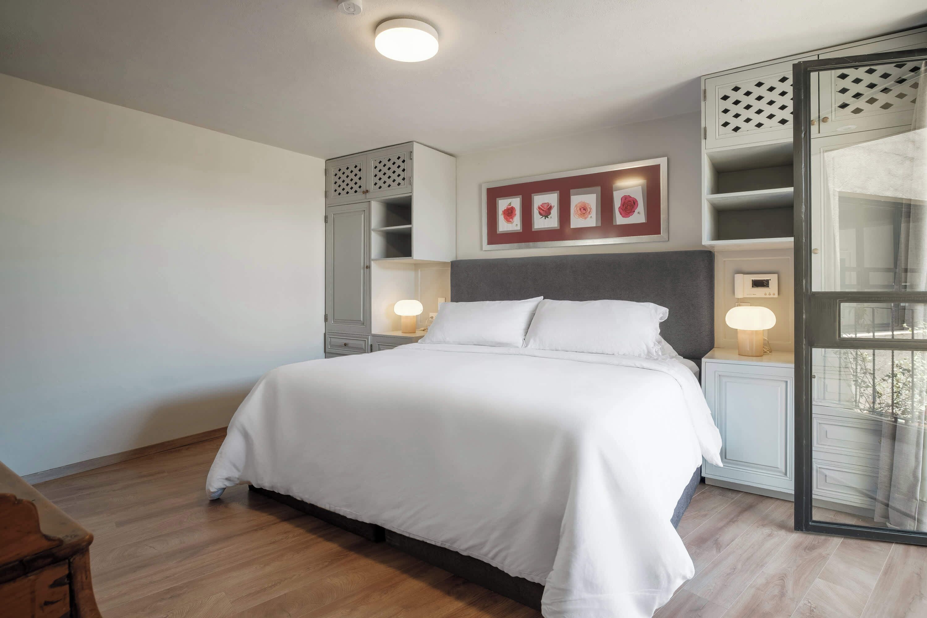 Un dormitorio con una cama grande, mesitas de noche con lámparas, un armario y un cuadro enmarcado en la pared.