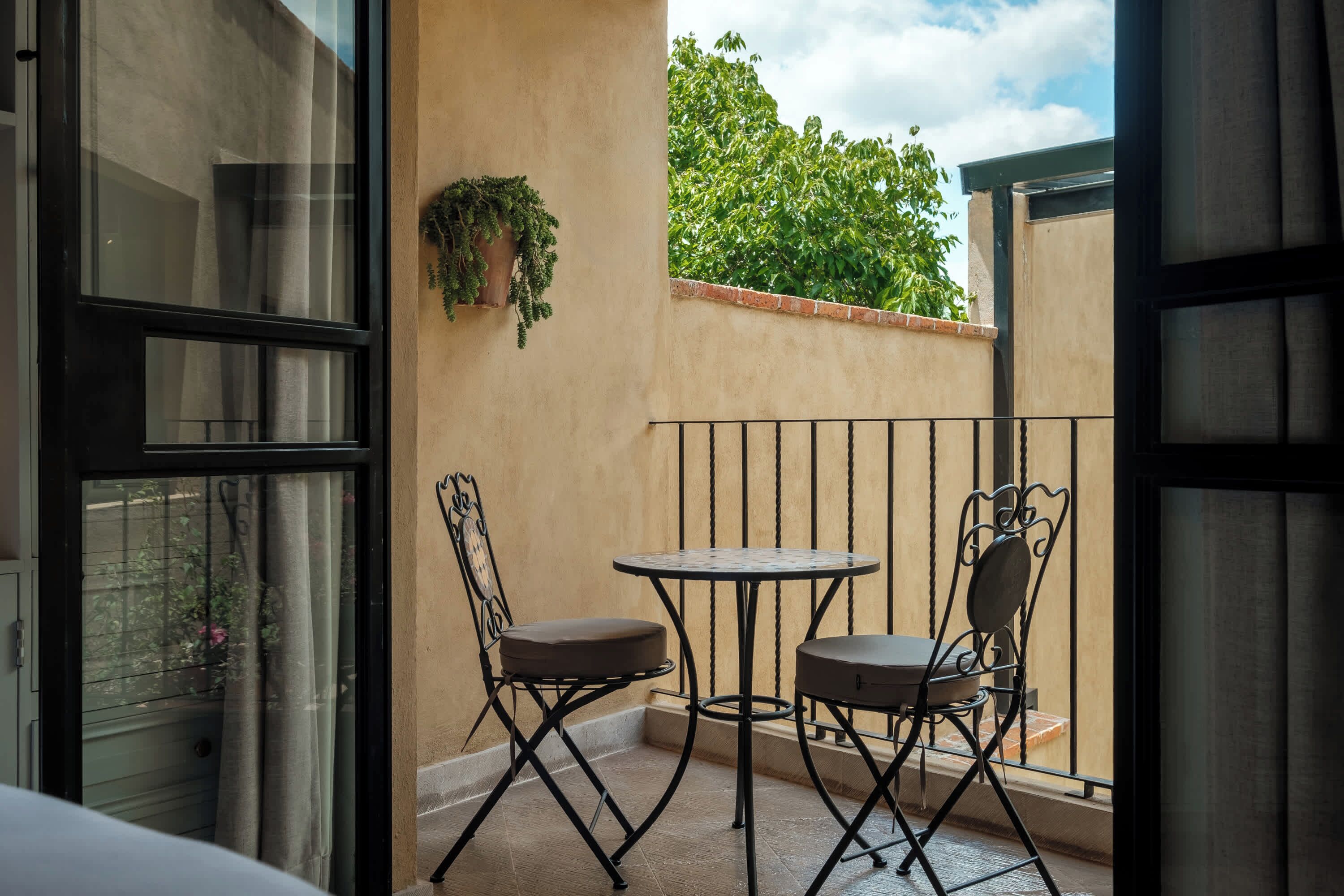 A balcony with a table and chairs, a potted plant, and a view of greenery.