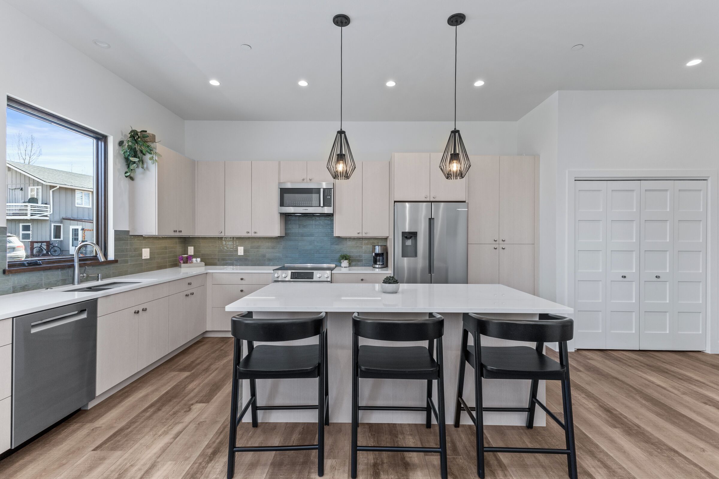 Una cocina moderna con una isla central, taburetes de bar, electrodomésticos de acero inoxidable e iluminación colgante.