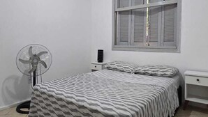 Une chambre à coucher avec un lit, un ventilateur de plafond, une fenêtre et une table de chevet.