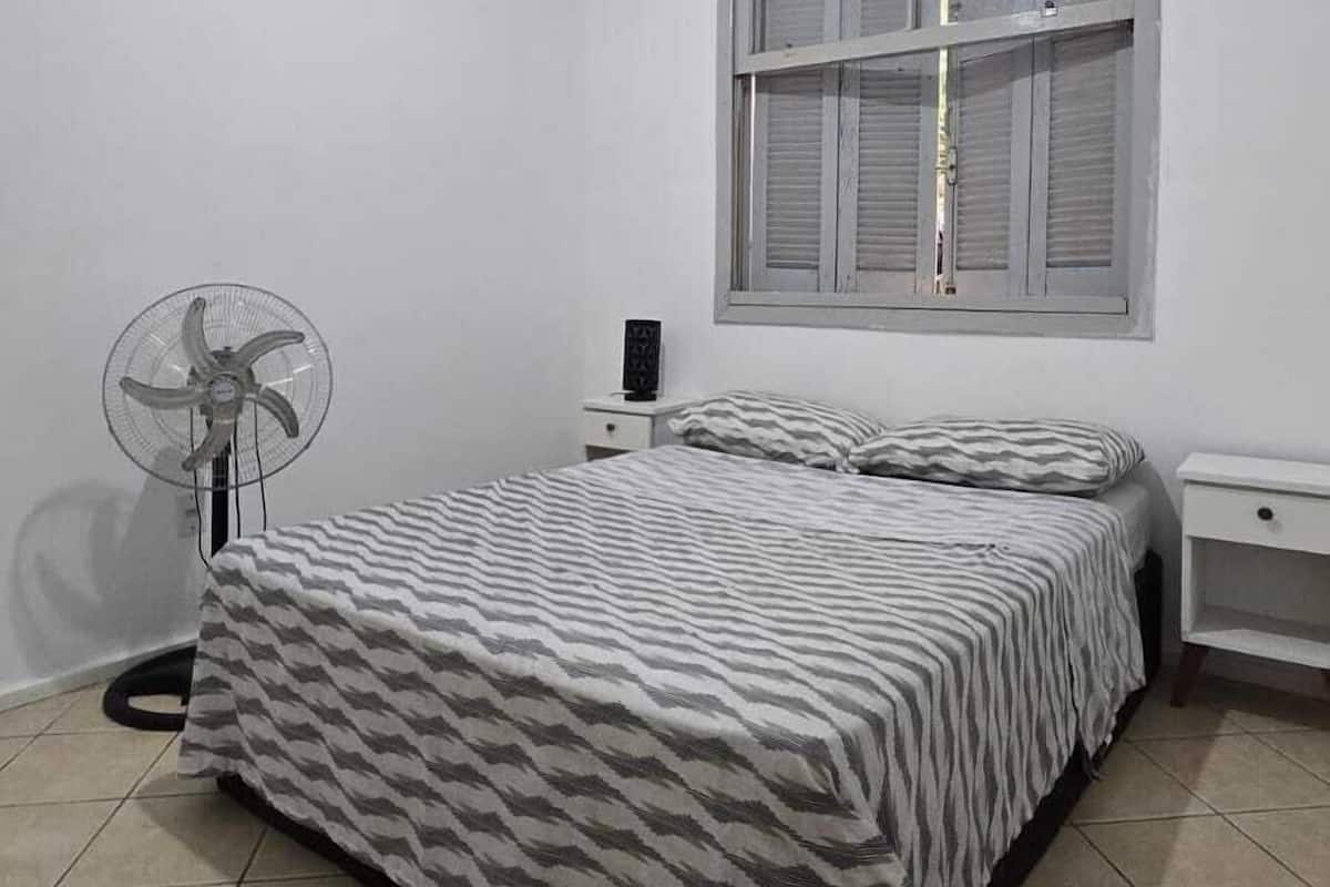 Een slaapkamer met een bed, een plafondventilator, een raam en een nachtkastje.